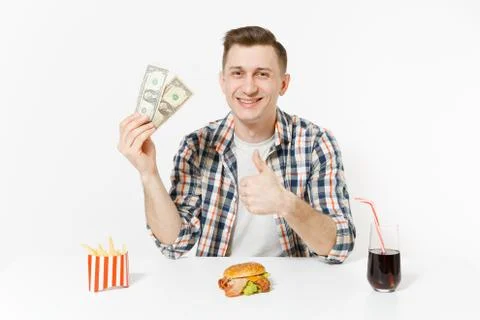 Poor fun man sitting at table with two dollar bills, burger, french fries, co Foto stock