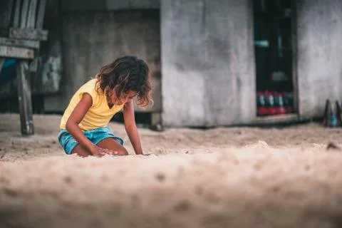 Poor kid with long hair playing with the sand of the beach Stock Photos