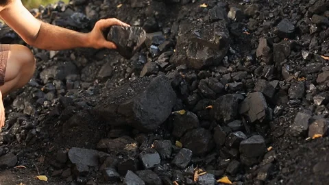 A poor middle-aged man crushes coal with his hands in a quarry for sale to Stock Footage 100389182
