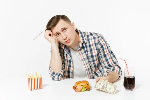 Poor sad man sitting at table with two dollar bills, burger, french fries, co Stock Photos
