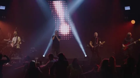 Pop group performs in front of cheering crowd on stage with bright multicolored Stock Footage 243935297