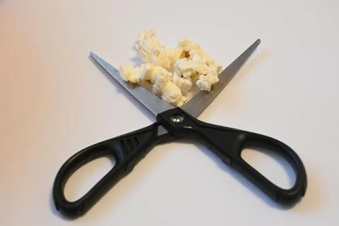 Popcorn and open scissors on a white surface Stock Photos