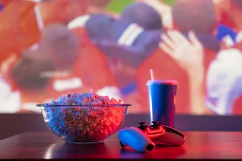 Popcorn in a bowl, a glass of soda water with a straw and a gamepad on a roma Stock Photos