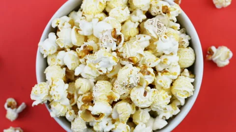 Popcorn is falling into a white bowl with red background.Top view Stock Footage 135679367