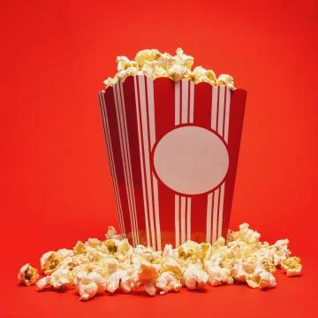 Popcorn in a large square box and around on a bright red background. Stockfoto's