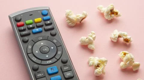 Popcorn on a light pink background next to a television remote control Stock Photos