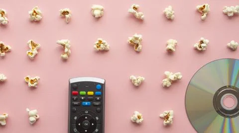 Popcorn on a light pink background next to a television remote control Stock Photos