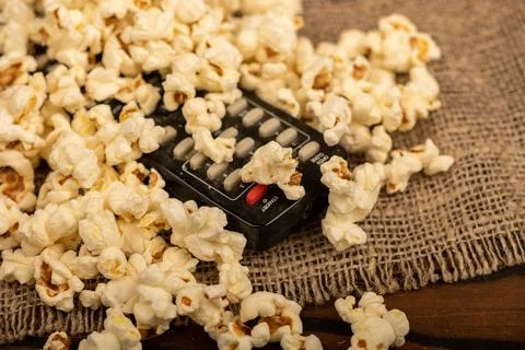 Popcorn scattered on the table and a remote control from the TV. Self-isolati Stock Photos