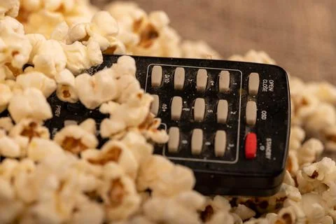 Popcorn scattered on the table and a remote control from the TV. Self-isolati Stock Photos