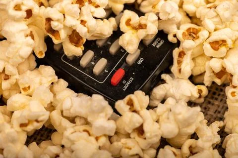 Popcorn scattered on the table and a remote control from the TV. Self-isolati Stock Photos