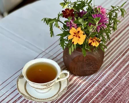 Porcelain cup of tea placed on a table next to a vase of flowers Stock Photos