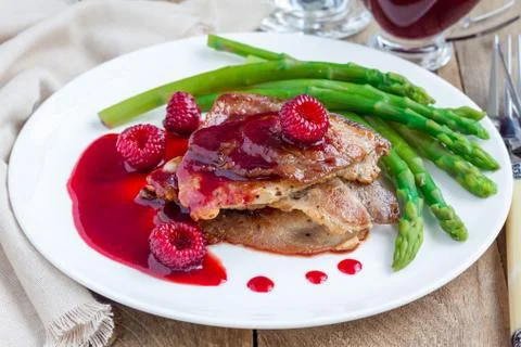 Pork cutlets with raspberry sauce and asparagus on white plate Foto stock