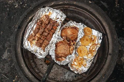 Pork kebab, pork steaks and onions are grilled on the foil over a campfire. Stock Photos