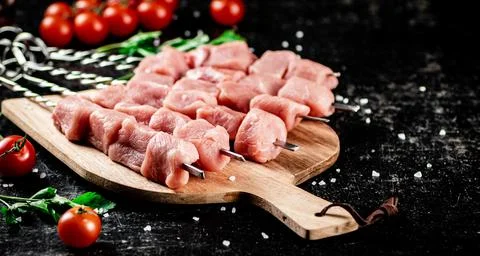 Pork kebab raw on a cutting board with tomatoes and parsley. Stock Photos