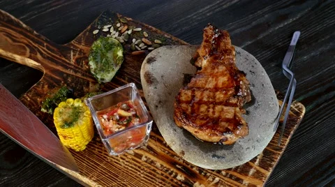Pork meat on the bone lying on a hot stone, sauce and grilled corn Stock Footage 52191980