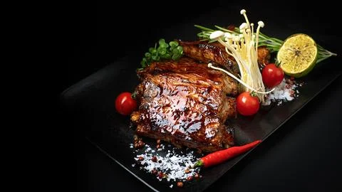 Pork ribs with cherry tomatoes, lime, mushrooms and herbs on black background Stock Photos