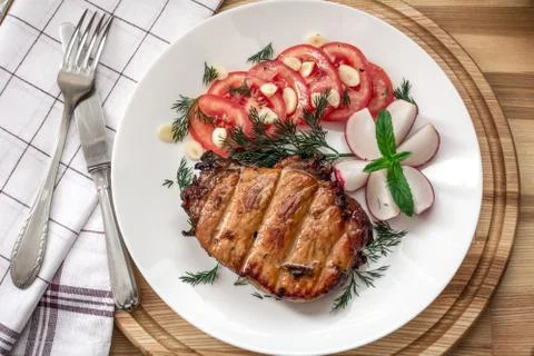 Pork steak cooked on the grill is decorated with a tomato, radish, dill, pars Stock Photos