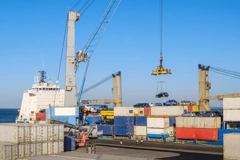 Port crane loading car into containers on bull carrier in port on sunny day Stock Photos