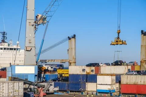 Port crane loading car into containers on bull carrier in port on sunny day Stock Photos