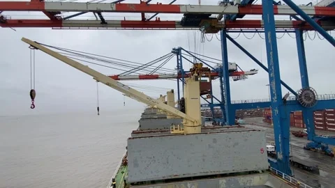 Port crane operation area beside the waterfront under an overcast sky. Stockbeeldmateriaal 345293715