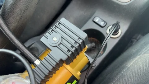 Portable electric air compressor operates inside a car while connected to the Vídeo Stock 337115143