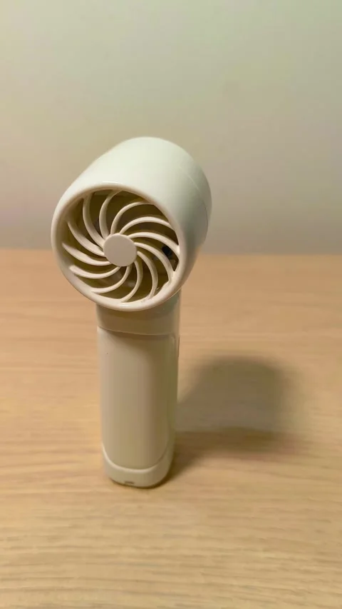 Portable mini fan providing instant cooling relief on a warm day, perfect for Video stock 318610751