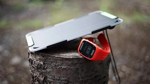 Portable solar panel charges a smartwatch on a tree stump in a summer day. Stock Footage 157456230