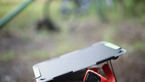 Portable solar panel charges a smartwatch on a tree stump in a summer day. Vídeo Stock 157456241