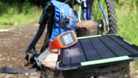 Portable solar panel charges a smartwatch on a tree stump in a summer day. Stock Footage 157483871