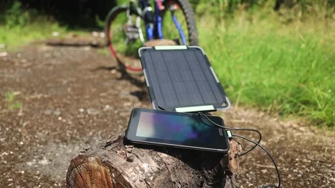Portable solar panel charges a tablet on a tree stump in a summer day. Stock Footage 157495771
