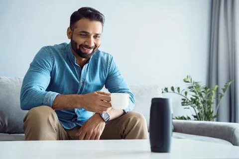 Portable wireless speaker assistant on table with man on sofa listening to music Stock Photos