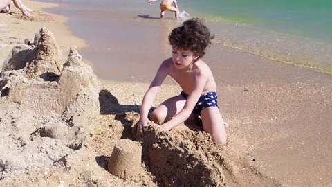 Portait of smiling dark-haired boy playing with sand on the beach Stock Footage 141335222
