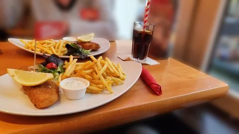 Portion of crispy breaded fish fillet with French fries served on a plate Stock Photos