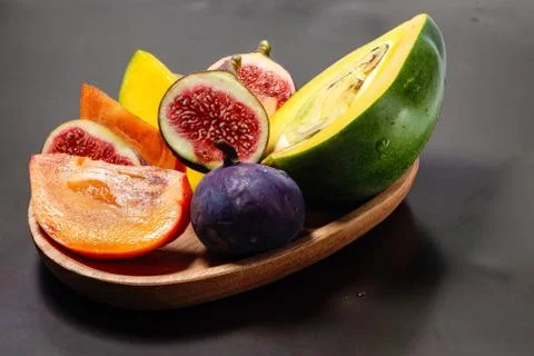 Portion of figs, persimmon and mango on a wood platter on black Stock Photos
