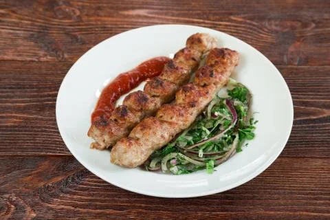 Portion luleh kebab on a plate. Appetizing dish on the wooden brown table. Stock Photos