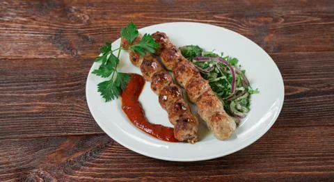 Portion luleh kebab on a plate. Appetizing dish on the wooden brown table. Stock Photos