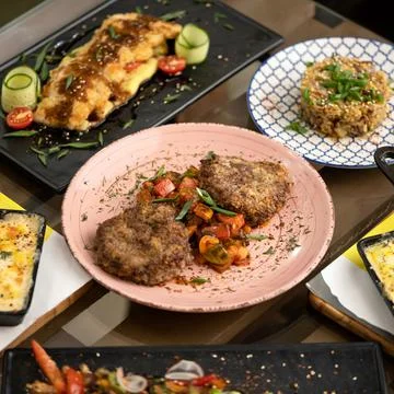 Portion of meat cutlets with vegetables, surrounded by variety of dishes Stock Photos