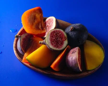 Portion of persimmon, figs and mango on a wood platter top view on blue Stock Photos