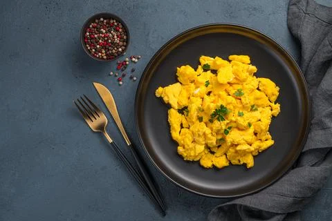 A portion of scrambled eggs with parsley on a dark background. Stock Photos