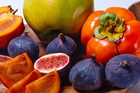 Portion of sliced figs, persimmon, apple  and mango on a wood platter on whit Stock Photos