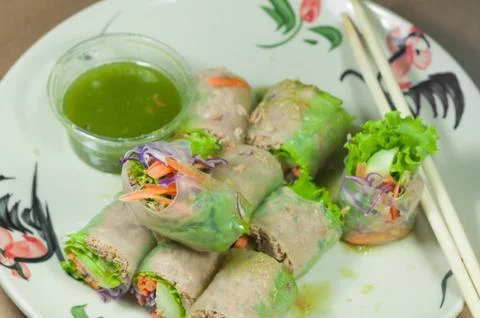 Portion of spring rolls on old wood with spicy sauce, vegetables and in noodl Stock Photos