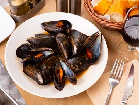 Portion of steamed mussels served with bay leaf on plate. Spanish dish mejillon Stock Photos