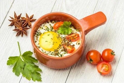 Portioned baked eggs in ceramic cocotte on white wooden table, breakfast. Stock Photos