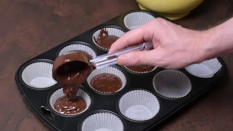 Portioning of chocolate muffin batter into paper molds in muffin tray. Stock Footage 243858751