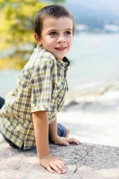 Portrait of 9 year old boy smiling with colorful shirt sitting on a wall Stock Photos