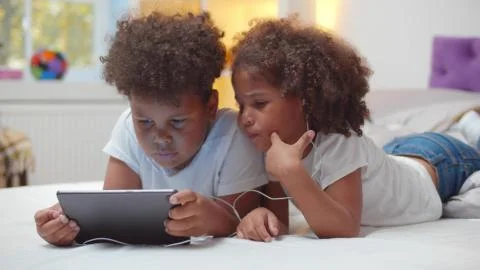 Portrait of adorable african boy and girl kids watching cartoon in earphones on Stock Photos