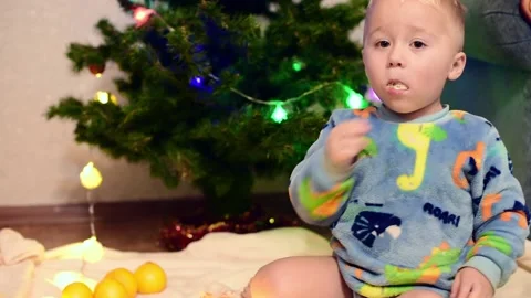 Portrait of adorable boy of two years eating tangerines . Magic vibe of new year Stock Footage 220520384