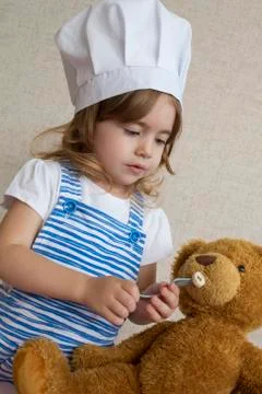 Portrait Adorable little girl in chef hat. baby feeds a toy bear Stock Photos