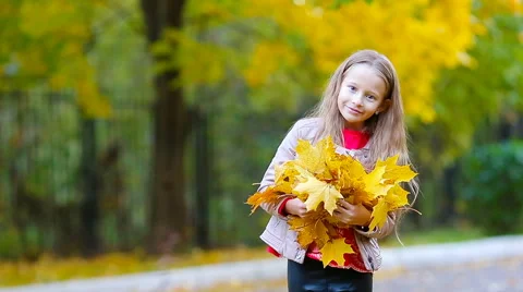 Portrait of adorable little girl with yellow and orange leaves outdoors at Stock Footage