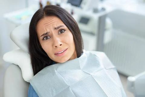 Portrait of afraid female client sitting in dental chair Stock Photos